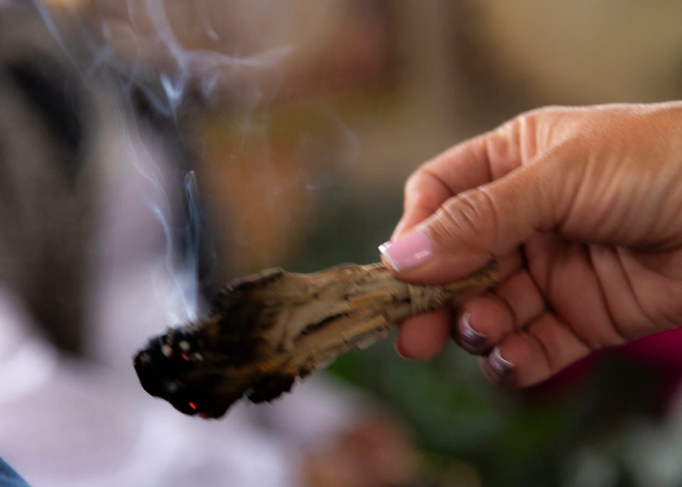 Mano sosteniendo una planta sagrada encendida que suelta humo