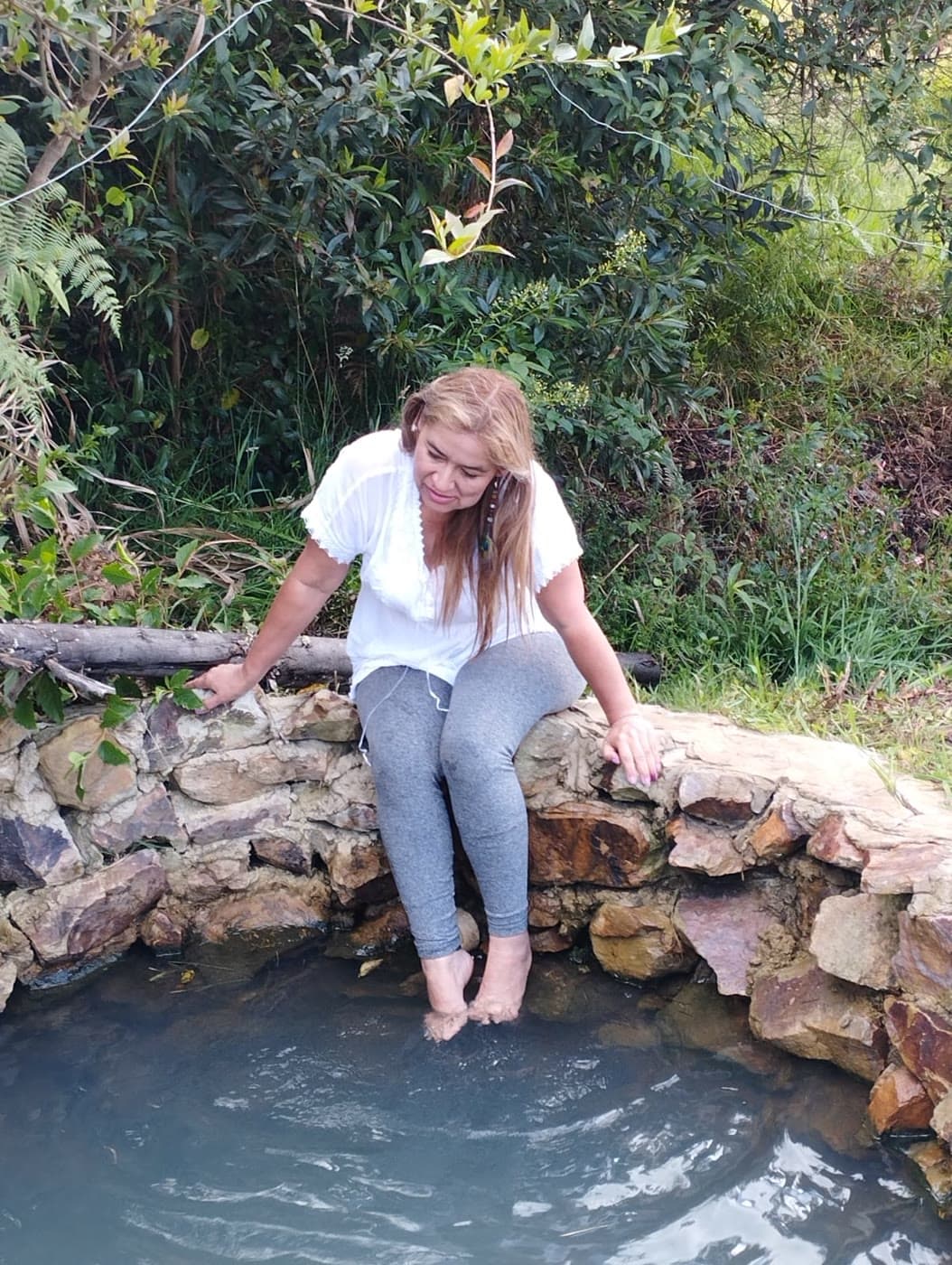 Mujer sentada al borde de la piscina natural con los pies en el agua